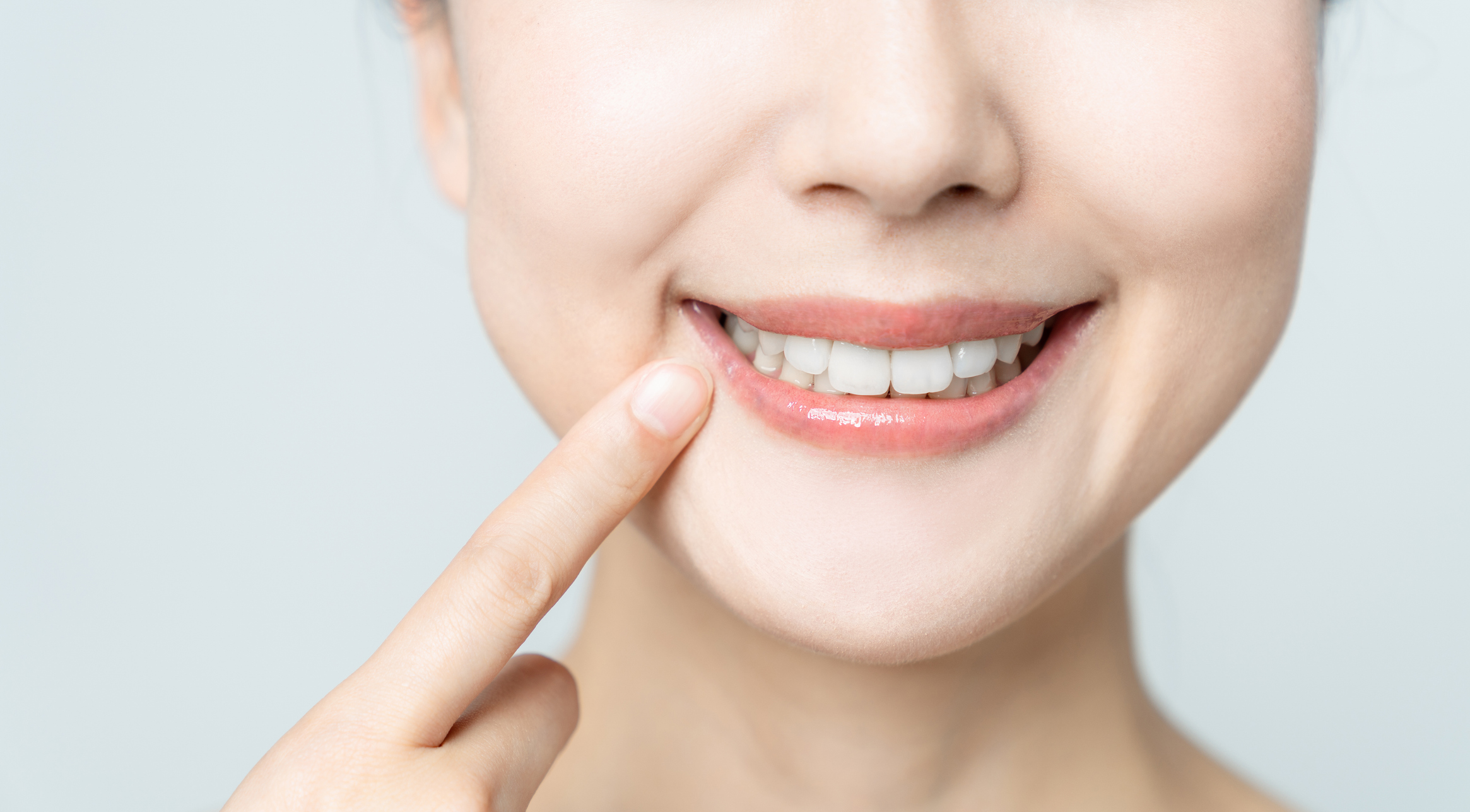 A woman smiling and pointing at her teeth with a light background.
