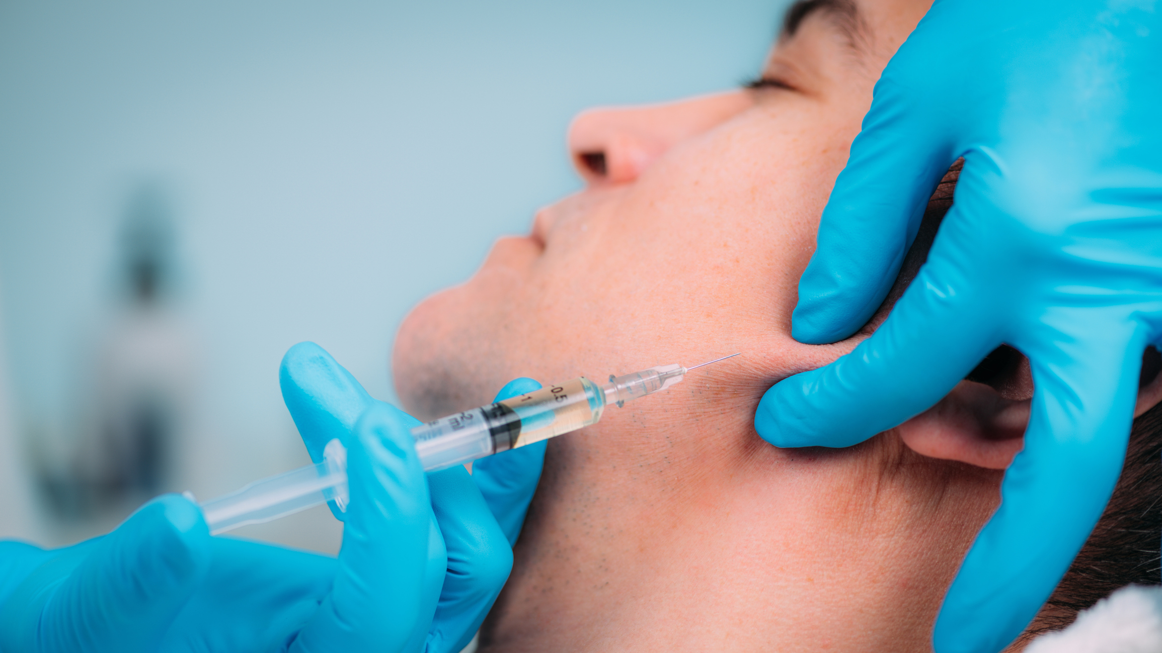 Healthcare professional administering an injection to a man's face with blue gloves.