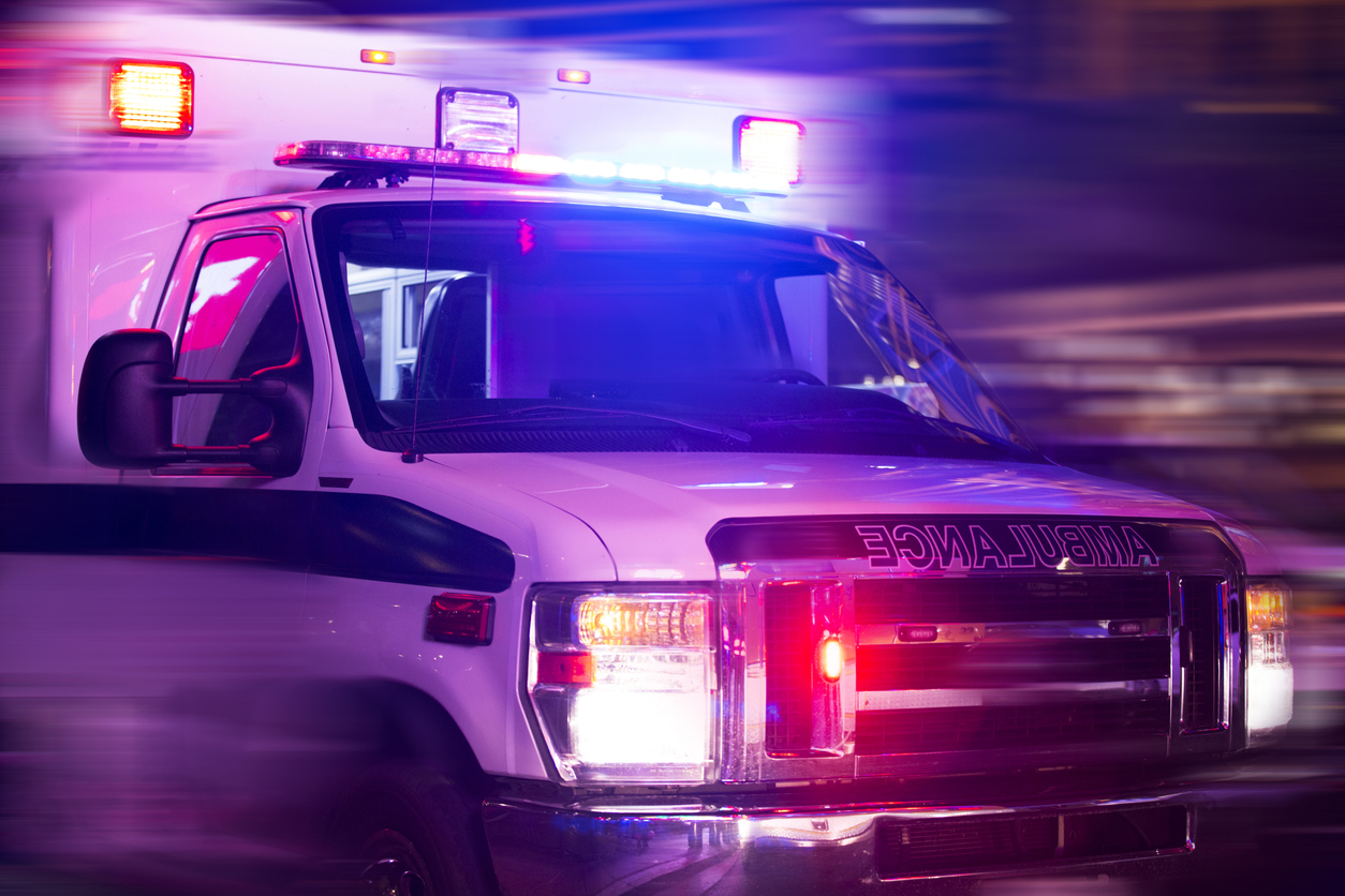 Front view of an emergency ambulance vehicle with flashing lights at night.